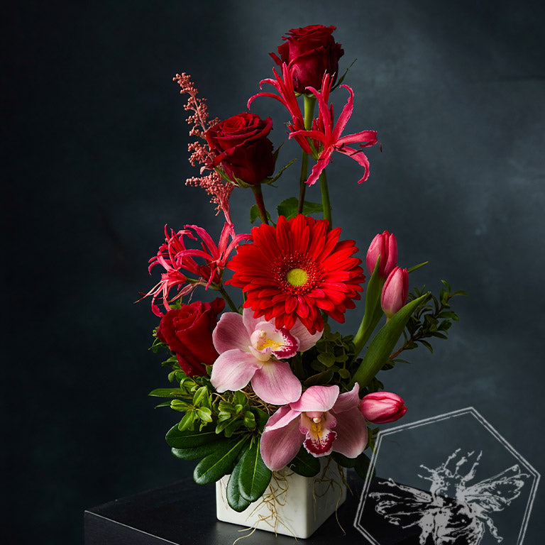 Romantic roses greenery, button mums and giant orchids nestled in lily grass accents in a white ceramic pot