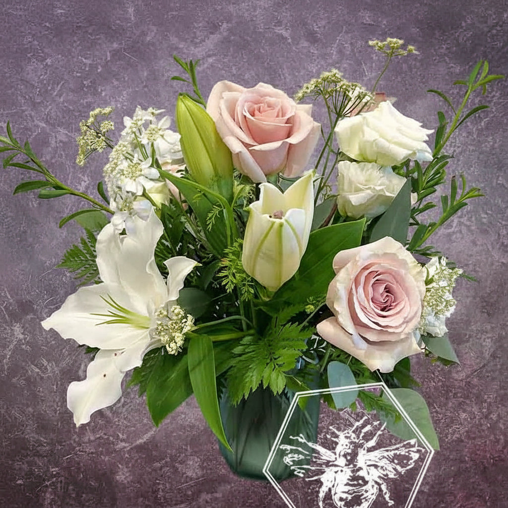 Traditional sympathy floral arrangement of white and pastel flowers in a glass vase accented by fresh tasteful blooms and complimentary greenery.