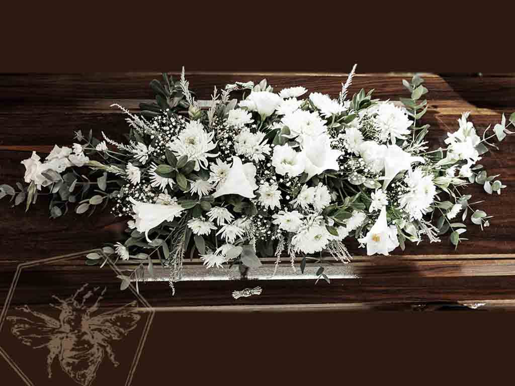 Brilliant white reverent casket spray on dark wooden casket 