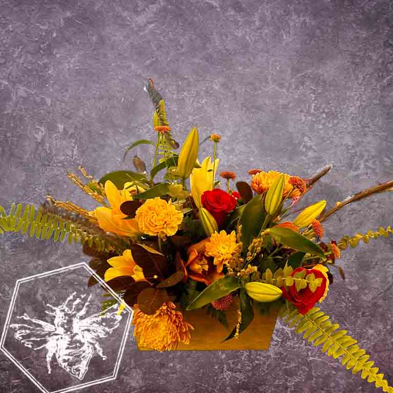 Colorful flower arrangement with yellow, red, and green flowers in a box against a gray background.