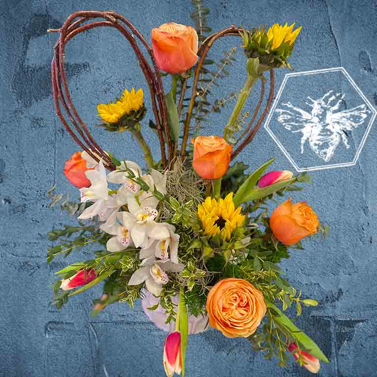 Colorful flower arrangement with orange roses, yellow sunflowers, and white orchids on a textured blue background.