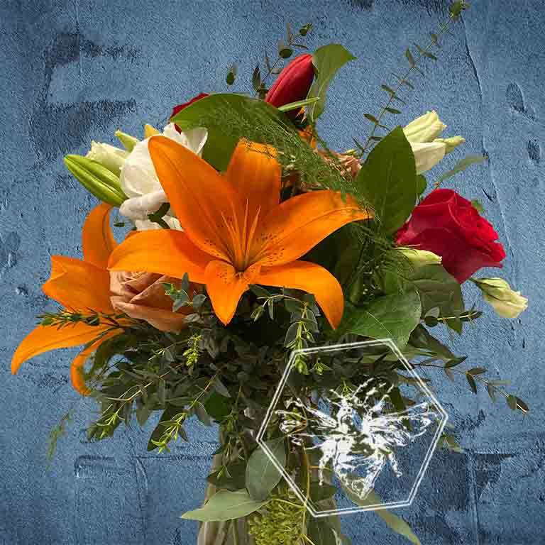 A bold, generous mix of vivid fresh flowers in a classic clear vase featuring lilies and roses and greenery
