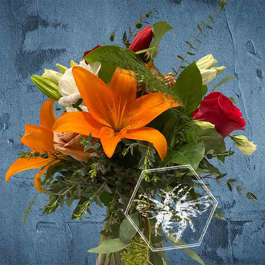 A bold, generous mix of vivid fresh flowers in a classic clear vase featuring lilies and roses and greenery