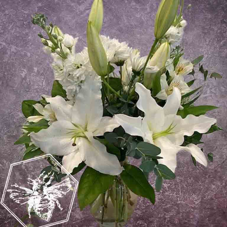 Bouquet of white lilies and other flowers in a clear vase on a textured gray background