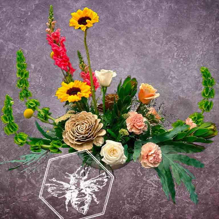 Luxurious modern arranged sunflowers featuring upward reaching garden snap dragons, white roses, elevated greenery and wooden rose accents.