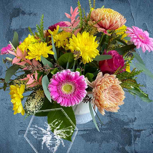 Colorful bouquet of flowers including yellow, pink, and orange flowers with green leaves on a textured blue background.