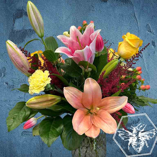 Bouquet of flowers with pink lilies, yellow roses, and other colorful flowers against a blue textured background.