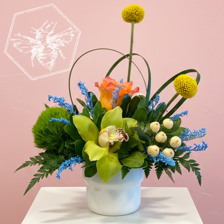 Romantic roses greenery, button mums and giant orchids nestled in lily grass accents in a white ceramic pot