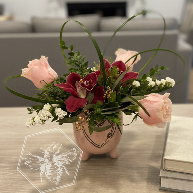 Romantic roses greenery, button mums and giant orchids nestled in lily grass accents in a white ceramic pot