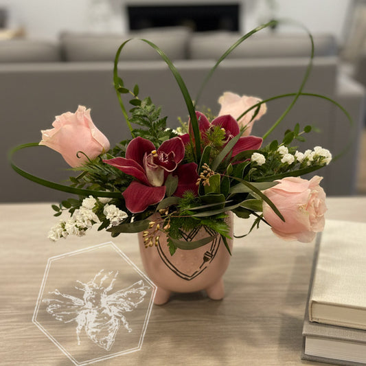 Romantic roses greenery, button mums and giant orchids nestled in lily grass accents in a white ceramic pot