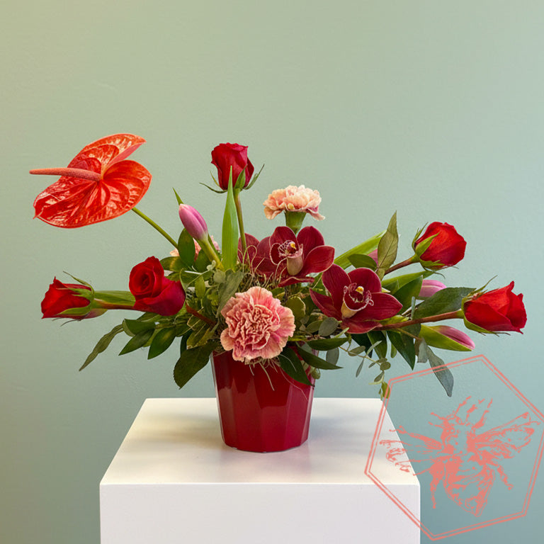 Modern arranged flowers with anthurium, roses fern, pussy willows and orchids with complimentary greenery in a ceramic pot