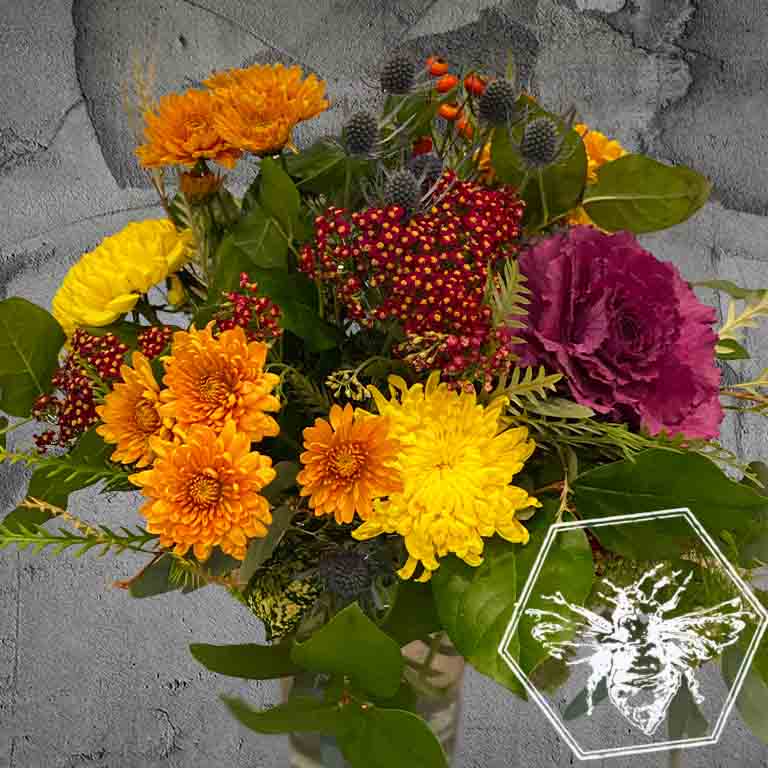 A bold, generous mix of vivid fresh flowers in a classic clear vase featuring kale, mums, eryngium and complimentary greenery