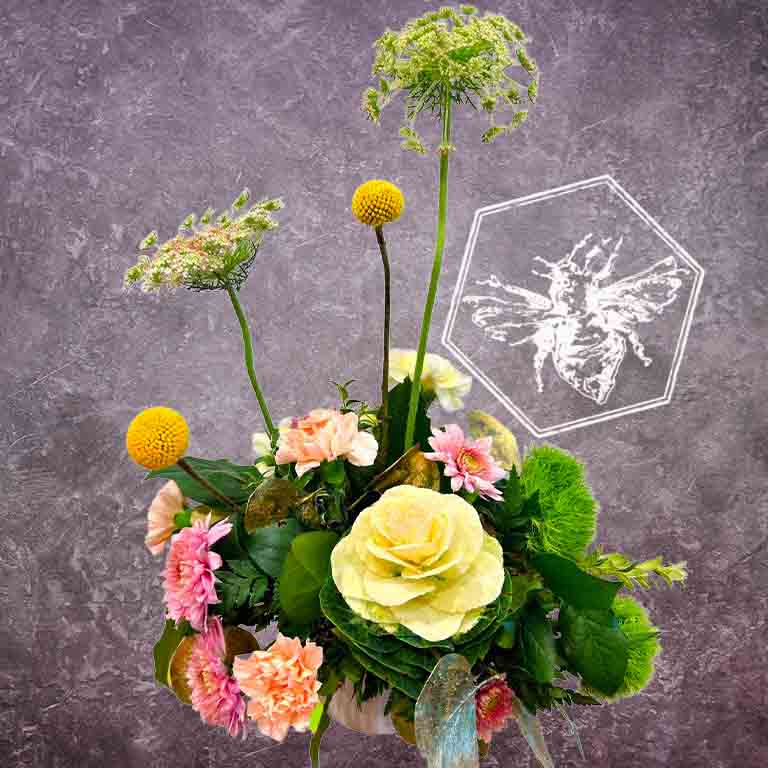 A modern, vertically styled sympathy floral arrangement in a neutral ceramic pot, featuring a lush mix of premium white and soft pastel blossoms accented with green foliage with splashes of floral color