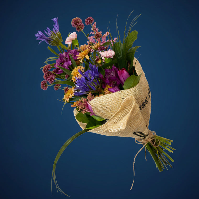Bouquet of colorful flowers wrapped in brown paper held against a gray background