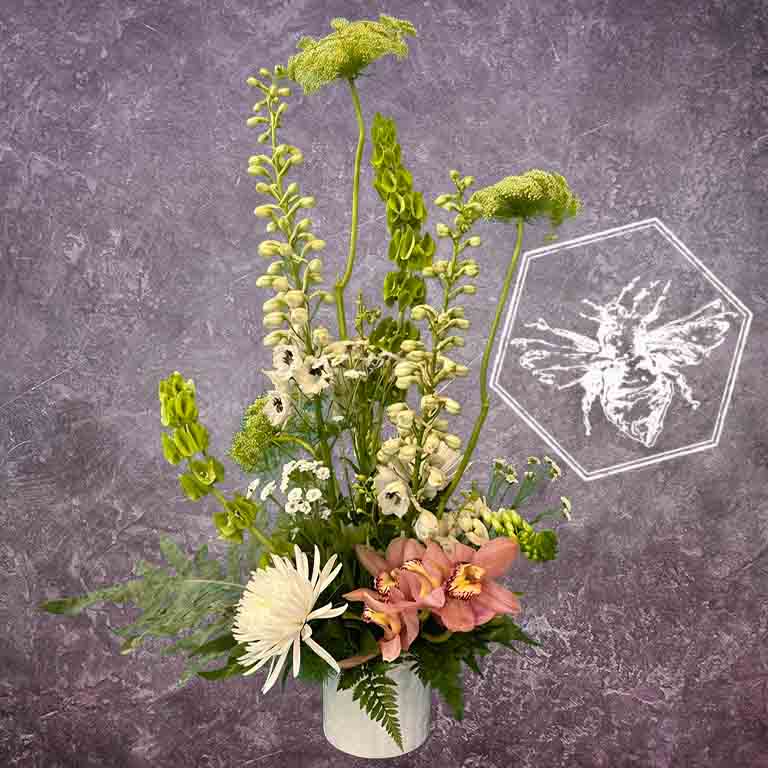 A modern, vertically styled sympathy floral arrangement in a neutral ceramic pot, featuring a lush mix of premium white and soft pastel blossoms accented with green foliage
