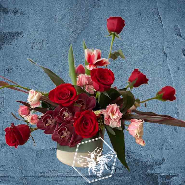 A modern arrangement of fresh cut roses with orchids, lisianthus and complimentary greenery.