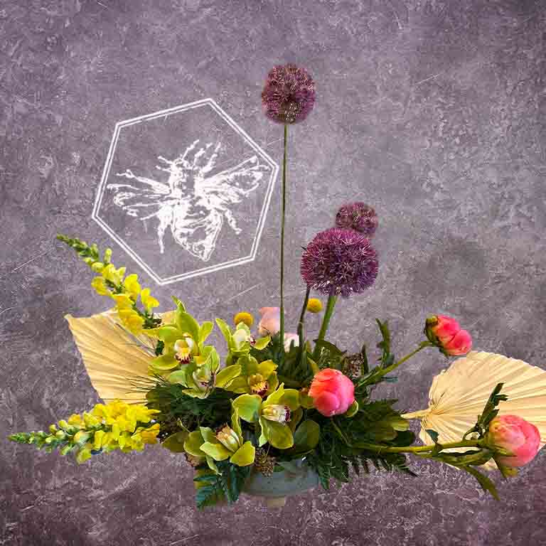 A modern, horizontally styled sympathy floral arrangement in a neutral ceramic pot, featuring a lush mix of premium white and soft pastel blossoms accented with green foliage featuring peonies and snap dragons.