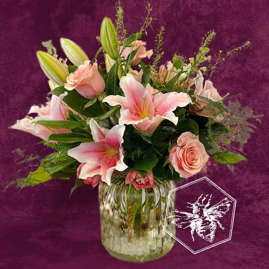 Bouquet of pink lilies and roses in a clear vase on a purple background