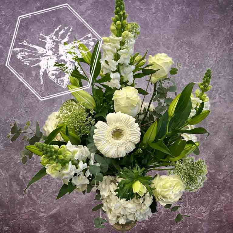 Traditional sympathy floral arrangement of white and pastel flowers in a glass vase accented by fresh tasteful blooms and complimentary greenery.