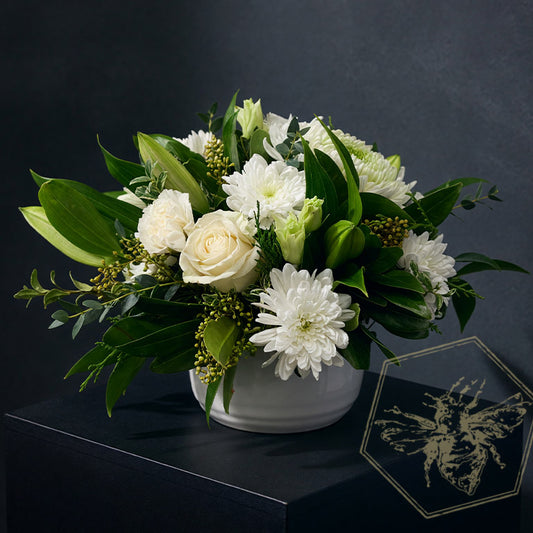 Compact modern flower arrangement with white roses and mums with complimentary greens  