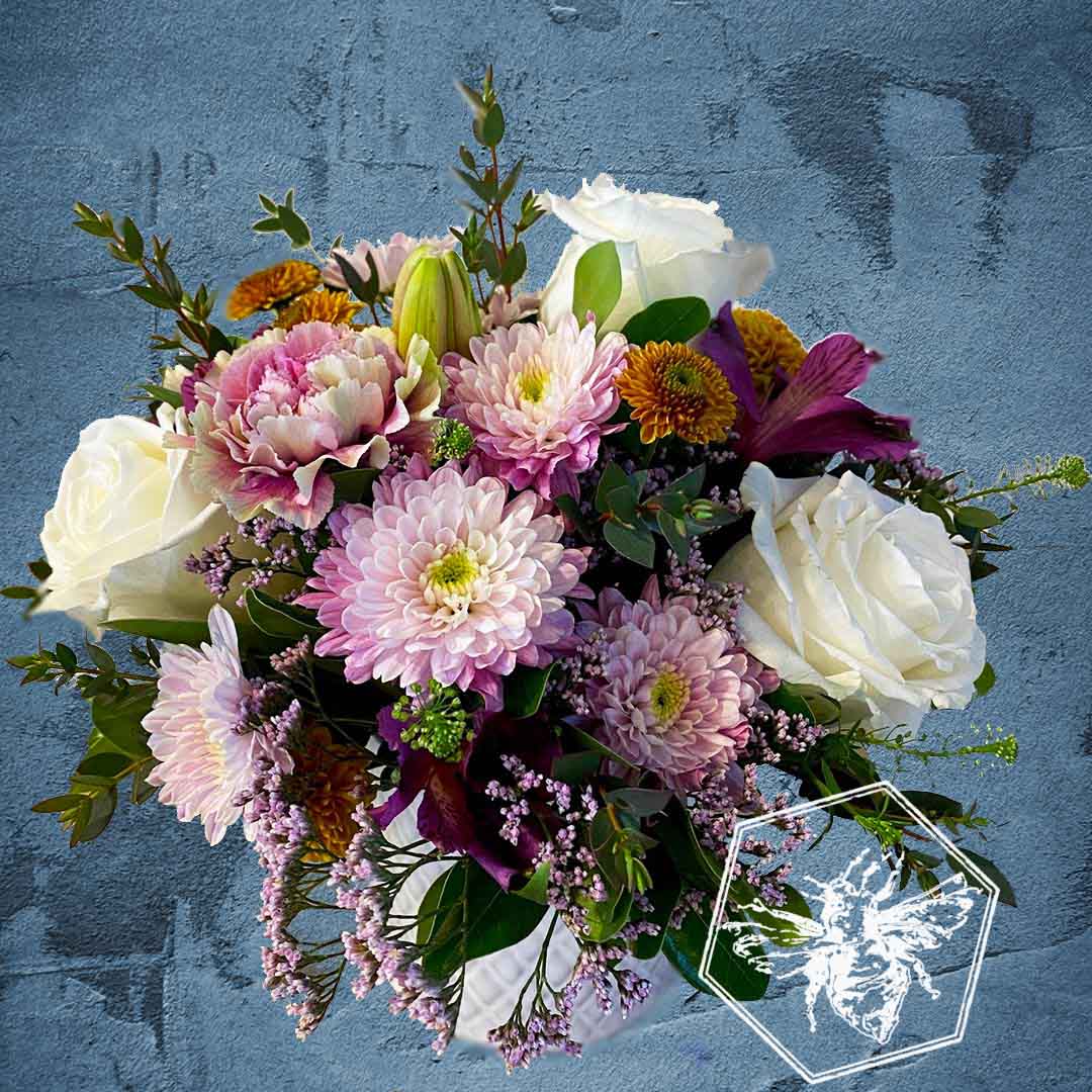 Compact arrangement of flowers with a blue textured background in a white ceramic pot.