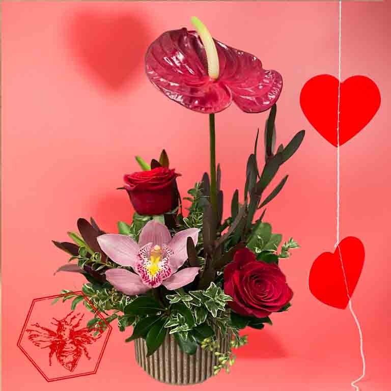 Floral arrangement with pink orchid, red roses, and greenery on a pink background with heart shapes.