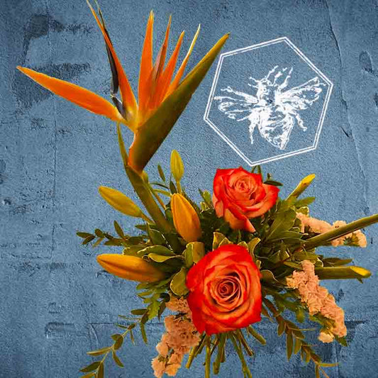 Tropical flowers with orange roses and a bird of paradise plant on a textured blue background.