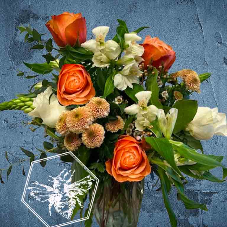A bold, generous mix of vivid fresh flowers in a classic clear vase featuring white star, button mums, roses, alstroemeria, and greenery