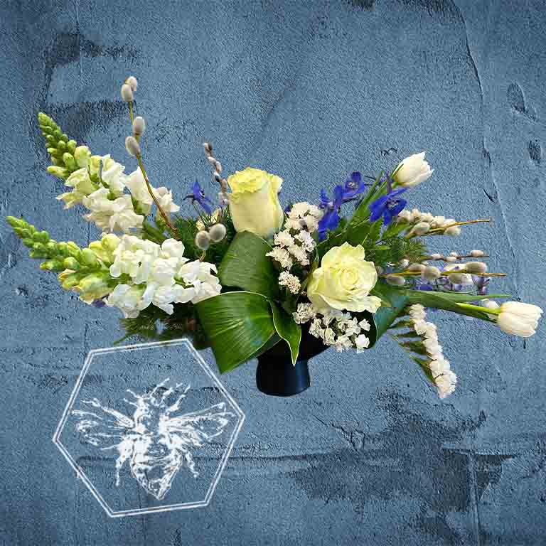 A modern, horizontally styled sympathy floral arrangement in a neutral ceramic pot, featuring a lush mix of premium white and soft pastel blossoms accented with green foliage