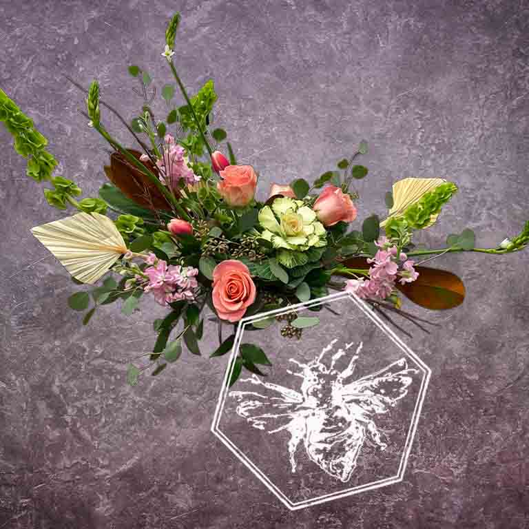 A modern, horizontally styled sympathy floral arrangement in a neutral ceramic pot, featuring a lush mix of premium white and soft pastel blossoms accented with green foliage, kale, roses and bells of Ireland