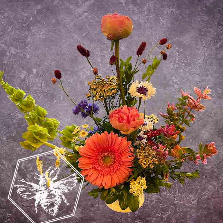 A modern, vertically styled sympathy floral arrangement in a neutral ceramic pot, featuring a lush mix of premium colorful blossoms accented with green foliage, bells of Ireland and garden blossoms